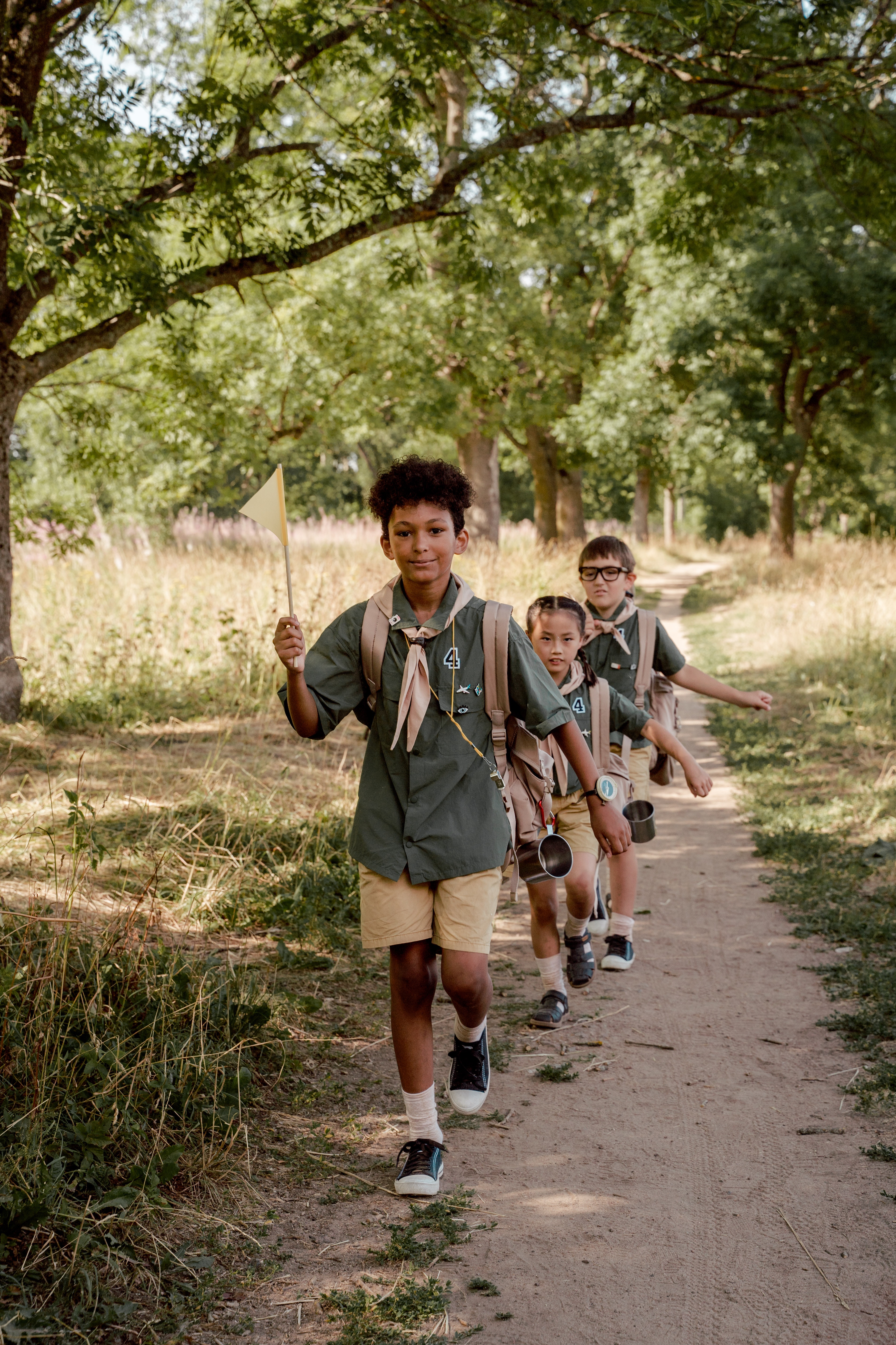4 kids in a row dressed in scouts outfits marching on a hiking path